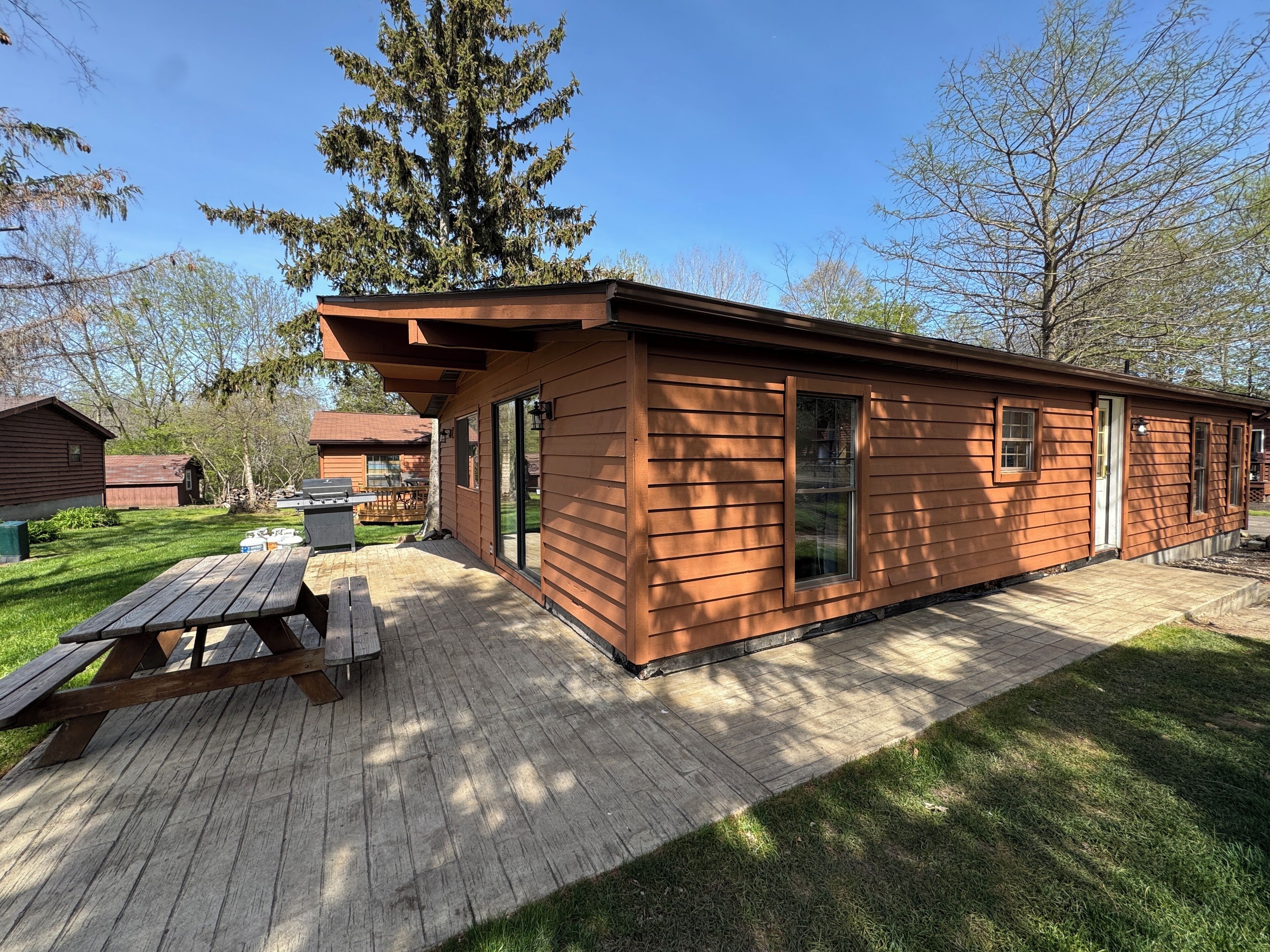 A wooden cabin with a patio, a picnic table, and a grill.