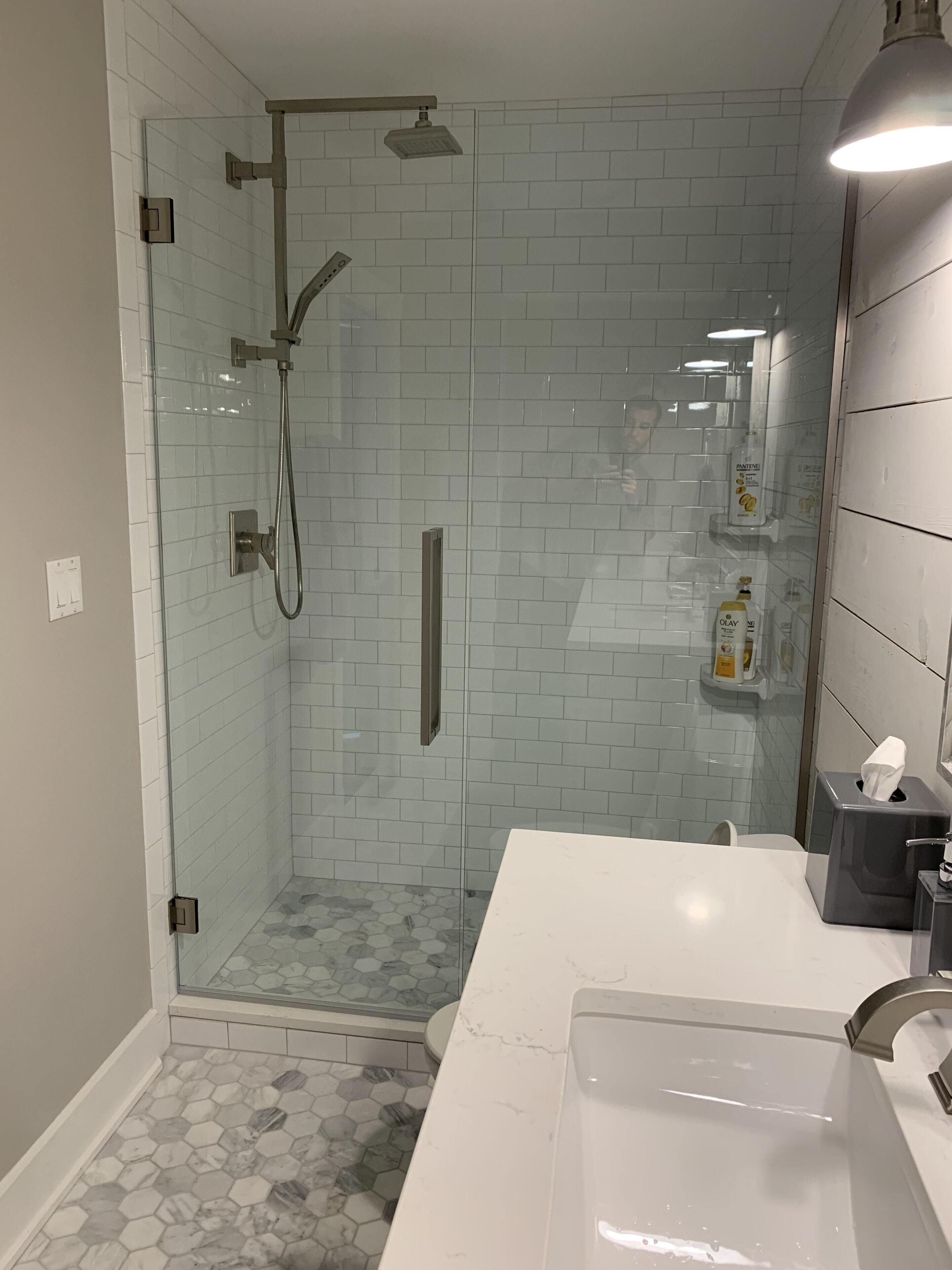 Un baño moderno con ducha de vidrio, lavamanos de mármol blanco y artículos de aseo en una estantería.