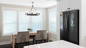 Eine moderne Küche mit einem großen, schwarzen Kühlschrank, weißen Schränken und einem Essbereich mit zwei Stühlen und einem Tisch.