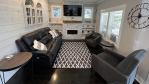 Ein modernes Wohnzimmer mit einem schwarzen Ledersofa, einem gemusterten Teppich, einem Kamin und einer großen Wanduhr.