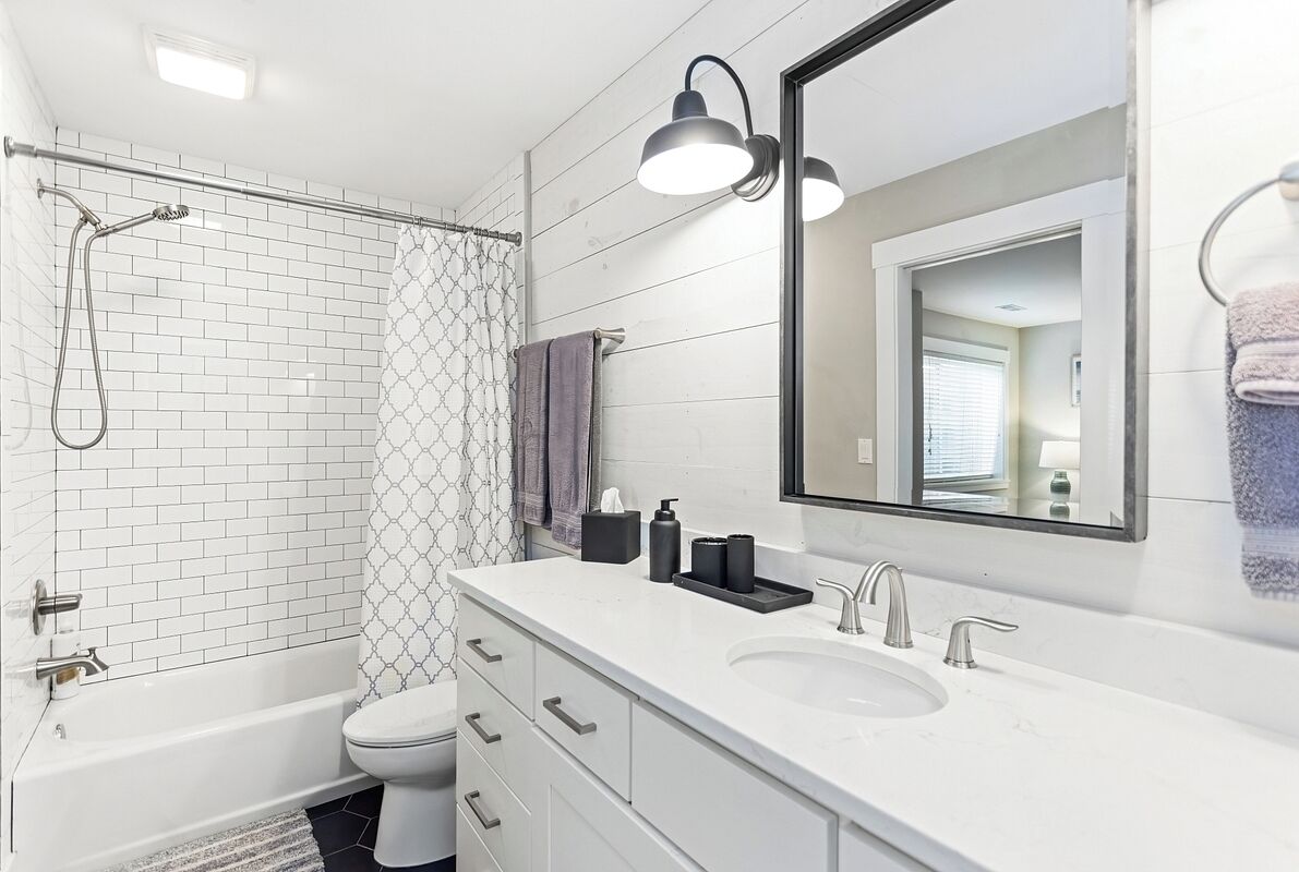 A modern bathroom with a white bathtub, a shower with a glass door, a large mirror, and a white sink with two faucets.
