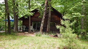 Een knus houten huisje met een veranda en een zitgedeelte buiten, omringd door bomen.