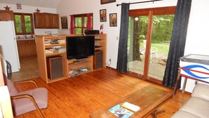 Een woonkamer met een televisie, houten kasten, een salontafel en uitzicht op een tuin door een schuifdeur.