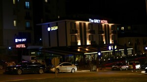 El Hotel Grey, con una fachada moderna, una entrada visible y un aparcamiento con coches.