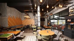 Un restaurante moderno con techos altos, vigas a la vista y una mezcla de mobiliario de madera y metal.