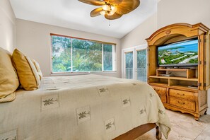 Un dormitorio con una cama, un televisor sobre un mueble de madera y una ventana con persianas.