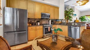 A modern kitchen with stainless steel appliances, wooden cabinets, and a dining area with a glass table and wicker chairs. - Tropical Escape at Mariner’s Club  2BR Key Largo Condo w/ Pools & Marina (Key Largo)