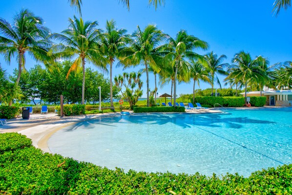 Una piscina rodeada de palmeras y sillas de descanso azules.