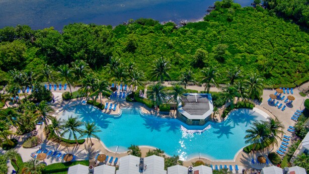 An aerial view of a resort with a central swimming pool, surrounded by palm trees and beach chairs. - Tropical Escape at Mariner’s Club  2BR Key Largo Condo w/ Pools & Marina (Key Largo)