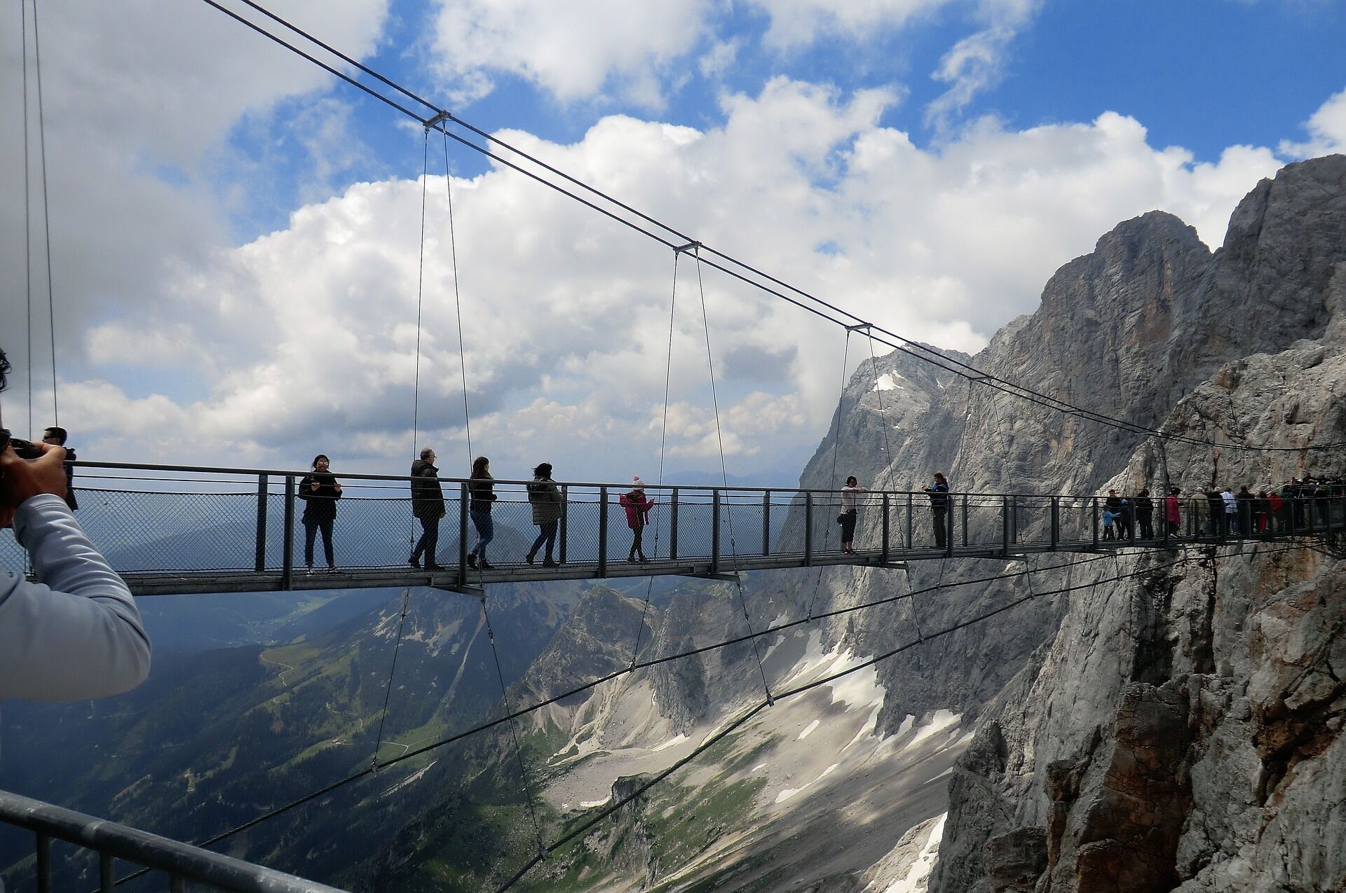 Un pont suspendu sur lequel des personnes se promènent, offrant une vue sur un paysage montagneux.