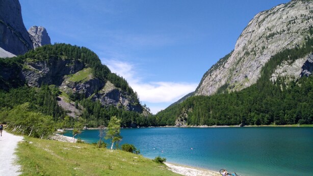 A mountainous landscape with a lake, a path, and a small boat. - Apartment Hallstatt Dachstein Inn (Gosau)