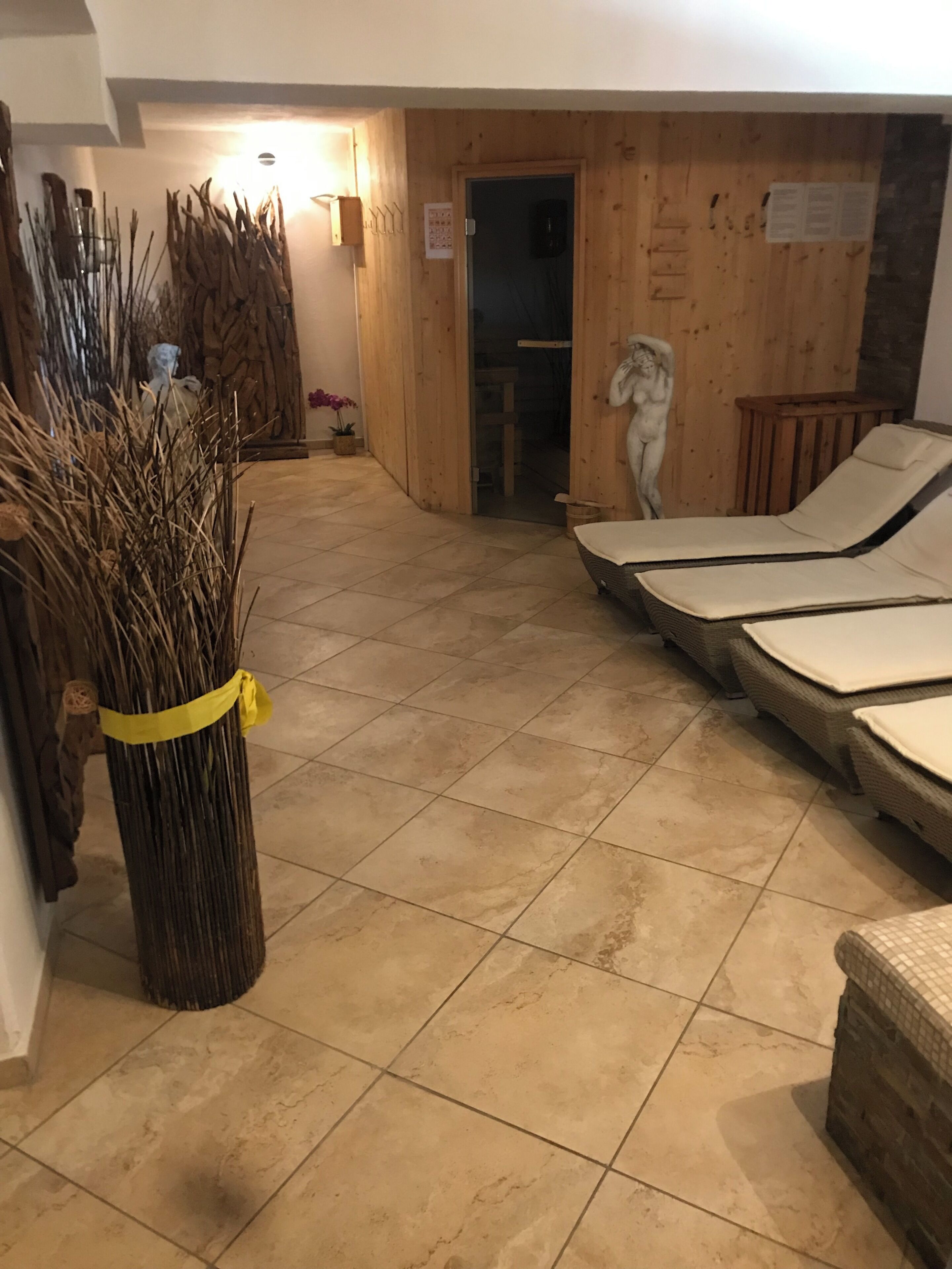 Ein Zimmer mit Fliesenboden, einem Korbsessel, einer Holztür und einer an der Wand befestigten Skulptur.