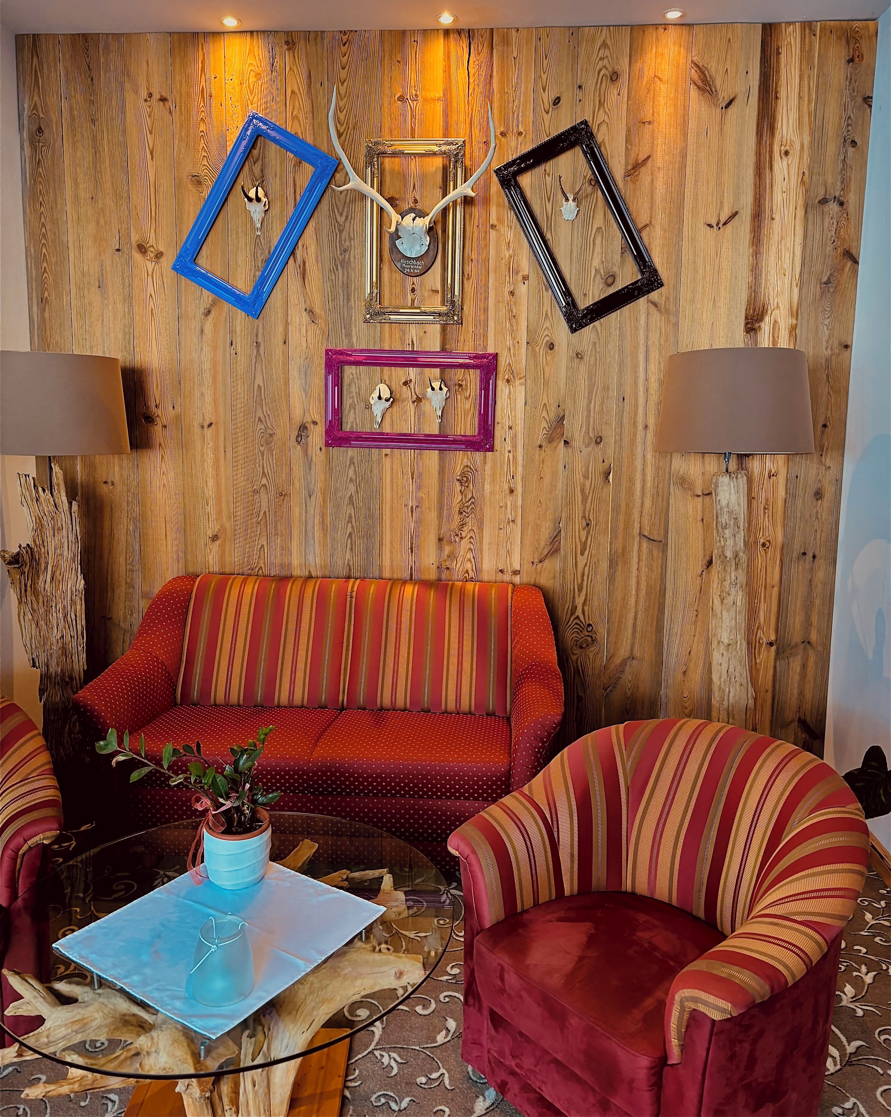 Una sala de estar acogedora con pared de madera, un sofá rojo, sillones a rayas y decoración en la pared.