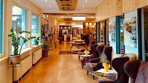 A hotel lobby with a wooden ceiling, large windows, and a seating area with armchairs. - Apartment Hallstatt Dachstein Inn (Gosau)