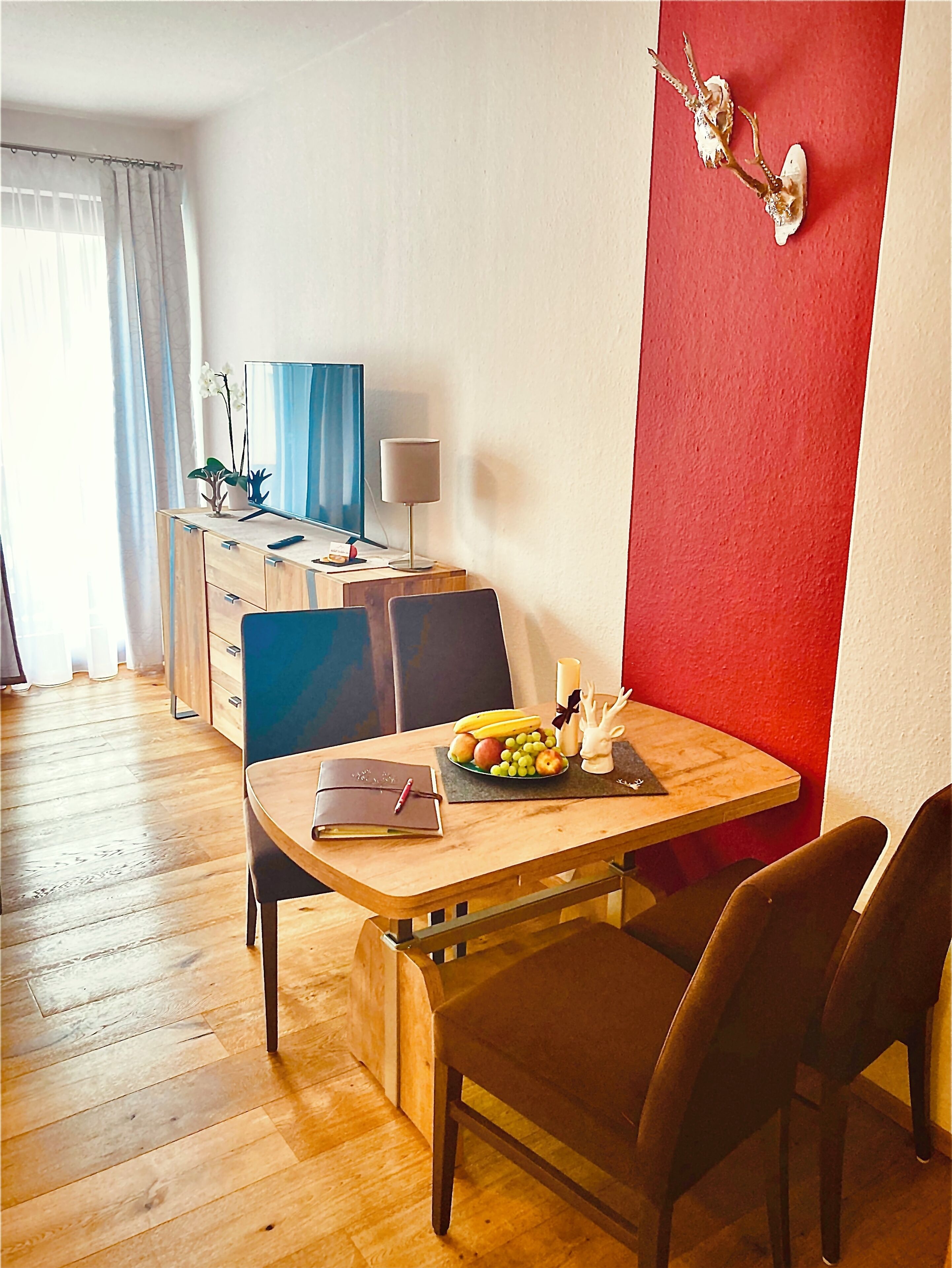 A dining area with a wooden table, chairs, a fruit bowl, and a laptop on the desk.
