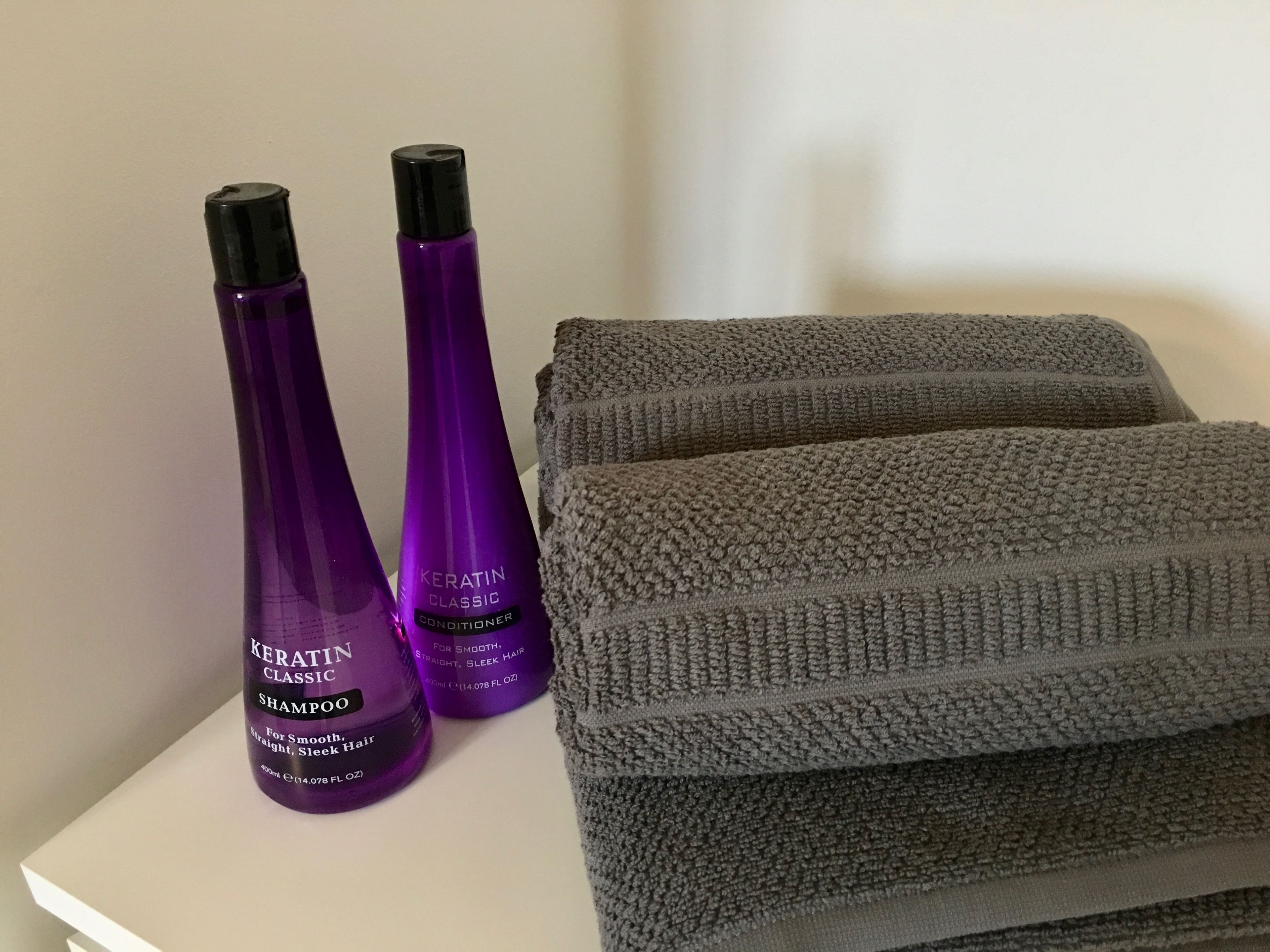 Two bottles of Keratin Classic shampoo and conditioner, and a folded gray towel on a white surface.