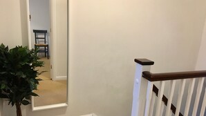 Eine Treppe mit weißen Geländern und einer dunklen Holzhandläufe, die zu einem Raum mit beigem Teppich und einem Blumentopf führt.