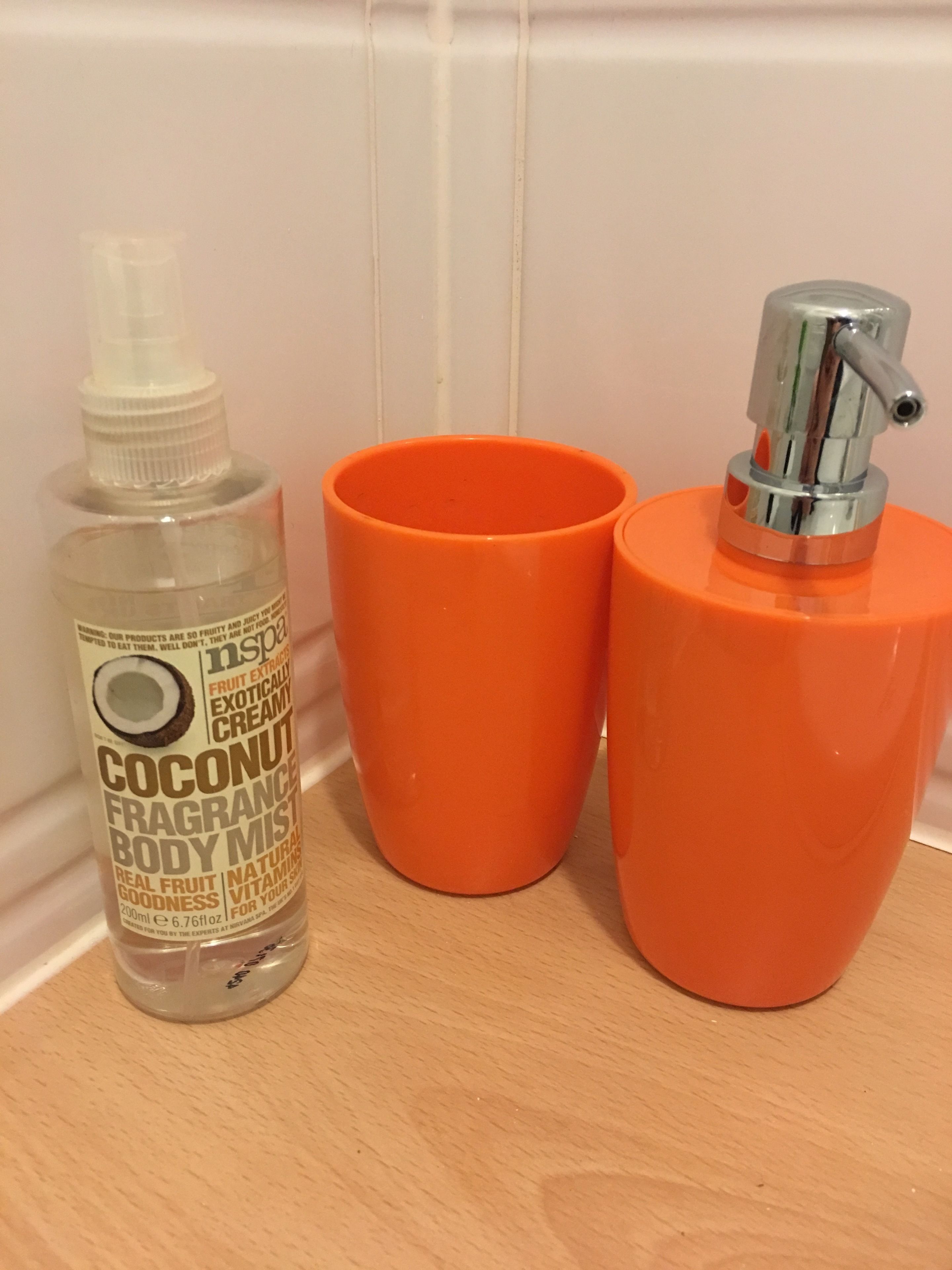 A bottle of coconut fragrance body mist and two orange cups on a wooden surface.