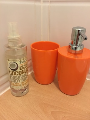 A bottle of coconut fragrance body mist and two orange cups on a wooden surface.