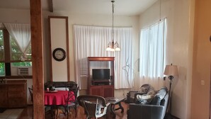 A living room with a wooden floor, a dining area with a red tablecloth, a black leather sofa, and a TV in a wooden entertainment unit. - Beautiful Loft Apartment Centrally Located for Recreation. (Union)