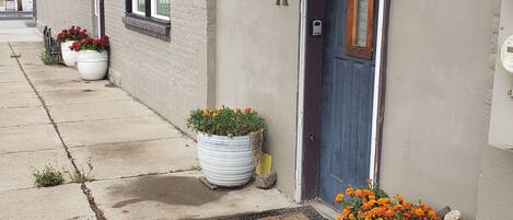 A building with a door marked 'A', large potted plants, and a metal awning.