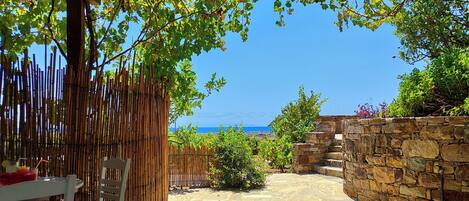 A covered outdoor seating area with a stone wall and a view of the sea.