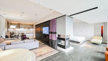 Une chambre d’hôtel moderne avec un coin salon, une cheminée, un lit et une cuisine en arrière-plan.