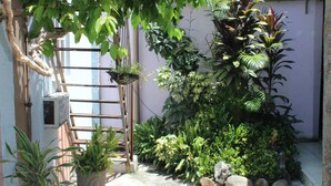 Un pequeño jardín al aire libre con plantas en macetas, una escalera de madera y una silla de plástico blanco.