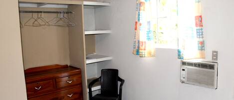 A bedroom with a bed, a wooden dresser, a chair, a wardrobe, and a window with a curtain.