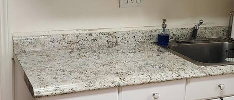 A kitchen with white cabinets, a granite countertop, a stainless steel sink, and a blue soap dispenser.