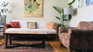 Un salon comprenant un canapé, un fauteuil à motifs, une table basse et un grand tableau abstrait accroché au mur.