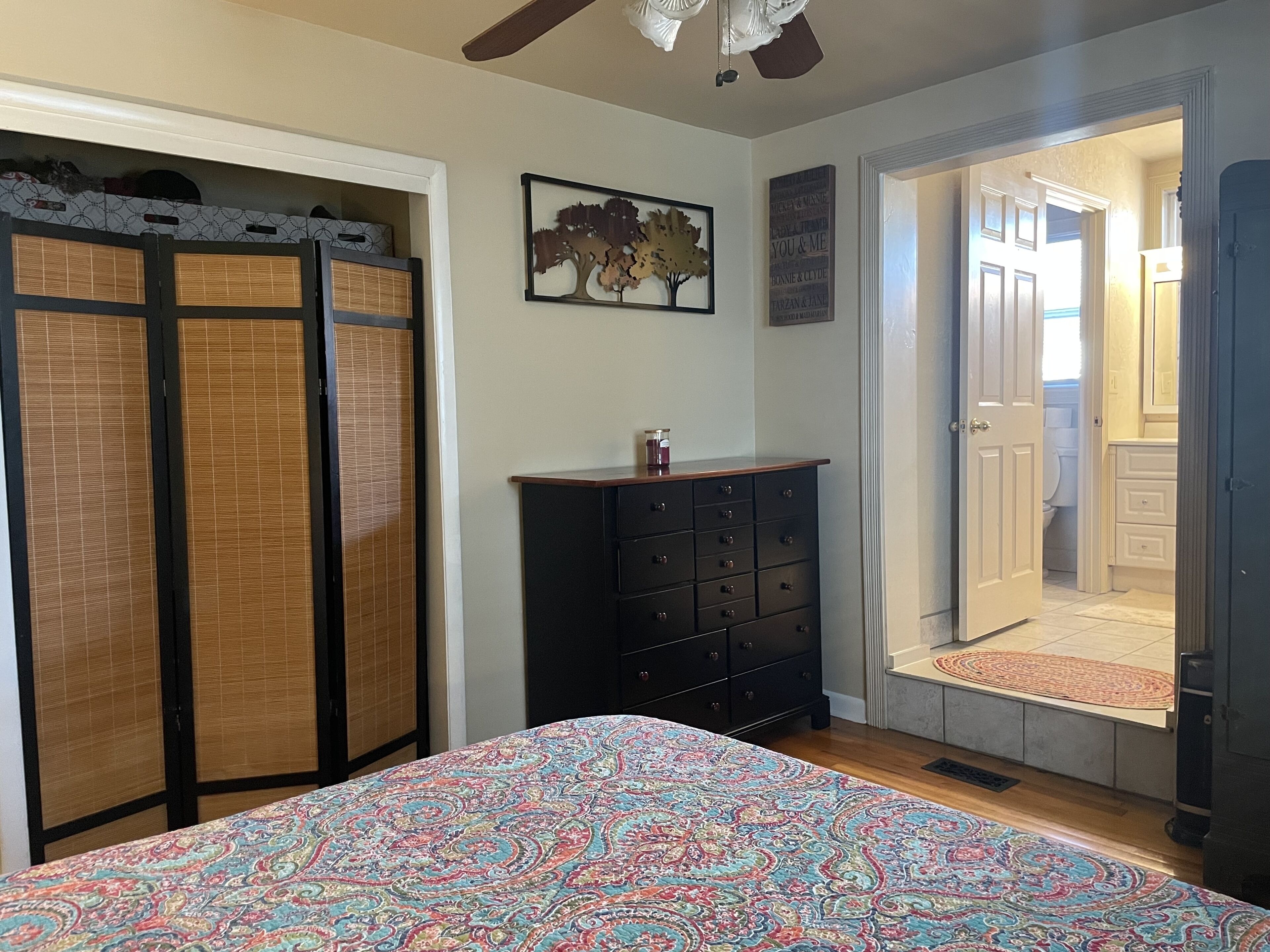 Ein Schlafzimmer mit einem Bett, einem Schminktisch, einem Shoji-Bildschirm, einem Deckenventilator und einer Tür zu einem Badezimmer.