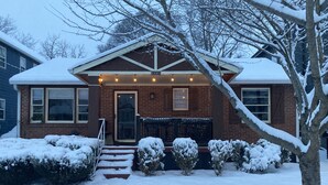 Une maison en briques dont le toit est recouvert de neige, avec des marches menant à la porte d’entrée.
