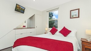 Ein Schlafzimmer mit einem Bett, einem Nachttisch, einem Schreibtisch, einem Spiegel und zwei Fenstern.