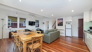 Eine moderne Küche mit Einbauofen und Kühlschrank, Holzboden und einer Essecke mit Holztisch und Stühlen.