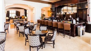 Un amplio vestíbulo de hotel con una zona de bar, asientos y una cocina al fondo.
