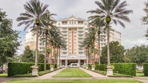 Un hotel grande y de varios pisos con una fachada simétrica, palmeras a lo largo de la parte delantera y un césped bien cuidado.