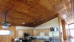 A kitchen with wooden cabinets, stainless steel appliances, and a dining area with white chairs. - Last Minute Special/ Elevator/Pool/Theater/Game Rm/Pool table/ping pong table (Nags Head)