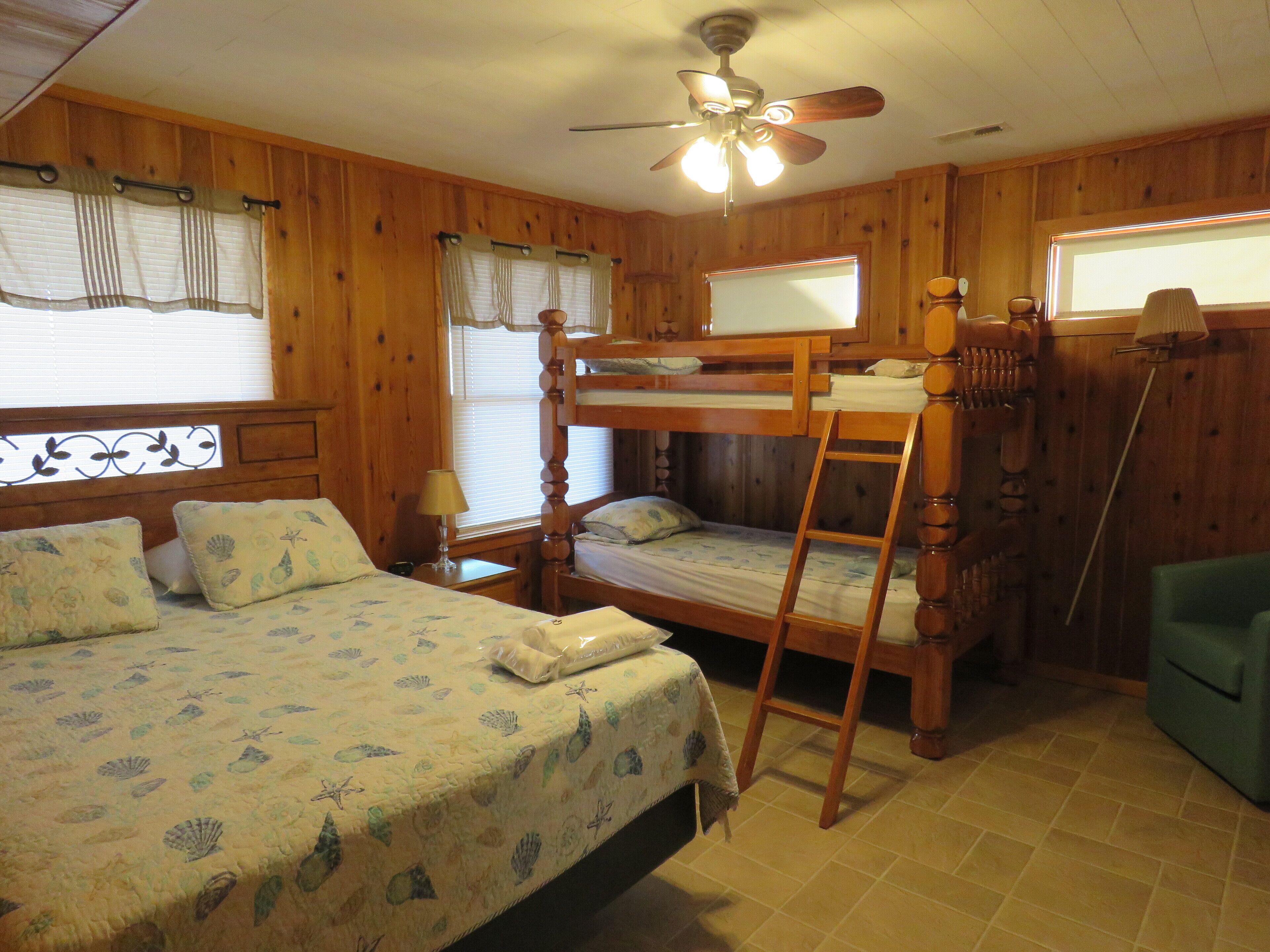 A bunk bed room with a wooden ceiling fan, a window with blinds, and a green chair.