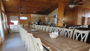 A long dining table with white chairs, a kitchen area with wooden cabinets, and a fireplace. - Last Minute Special/ Elevator/Pool/Theater/Game Rm/Pool table/ping pong table (Nags Head)