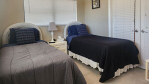A bedroom with two beds, a nightstand, a lamp, a window with blinds, and a door. - Bayshore Inn & Docks Two Bedroom Unit 8 Overlooking the Pool (Naples)