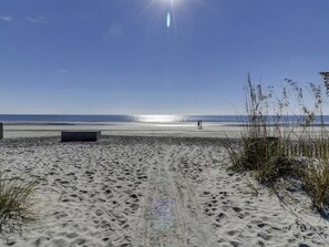 A sandy beach with footprints leading to the water, a clear sky, and a person walking in the distance. - Coastal Villa in Shorewood Complex w/ Amenities (Hilton Head Island)