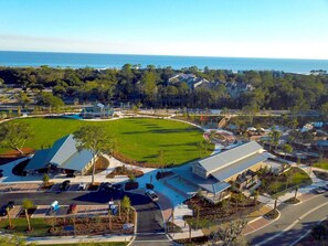 An aerial view of a golf course with a clubhouse, parking area, and surrounding residential buildings.