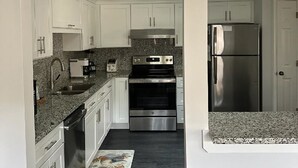 A modern kitchen with white cabinets, granite countertops, a stainless steel refrigerator, and a built-in oven. - Couples Cozy retreat, quiet and 10 minute walk to the beach -REMODELED NOV 2023 (Hilton Head Island)