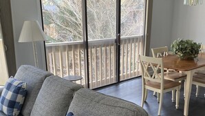 A living room with a grey sofa, blue and white checkered pillows, a dining table with chairs, and a balcony with a railing. - Couples Cozy retreat, quiet and 10 minute walk to the beach -REMODELED NOV 2023 (Hilton Head Island)