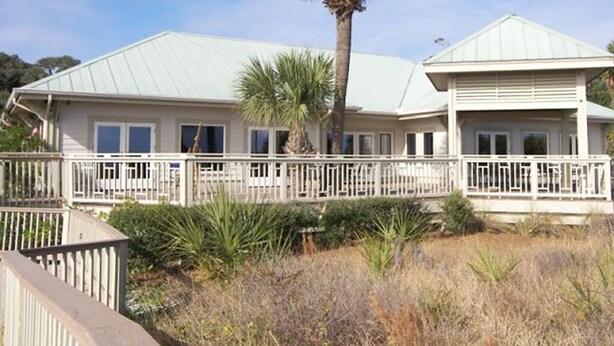 A two-story house with a white exterior, a covered porch, and a palm tree in the yard. - Couples Cozy retreat, quiet and 10 minute walk to the beach -REMODELED NOV 2023 (Hilton Head Island)