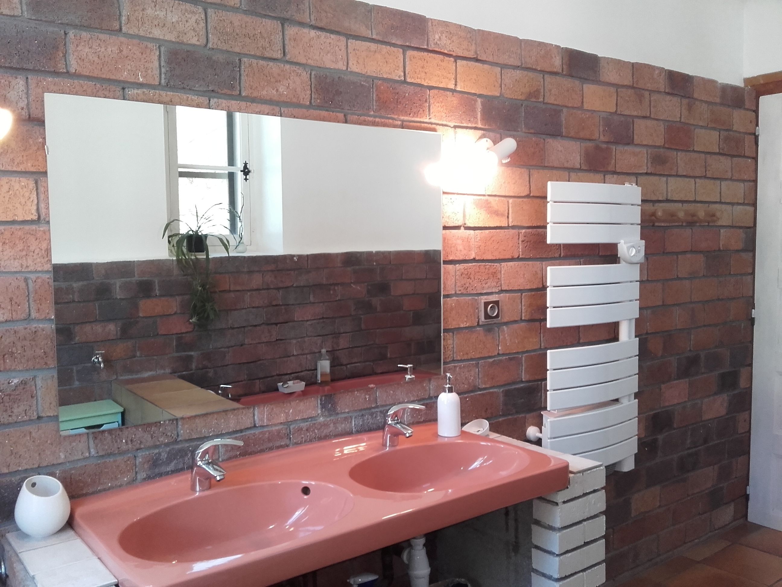 Un baño con dos lavamanos, un espejo grande y un perchero de toallas frente a una pared de ladrillo.