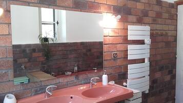 Un baño con dos lavamanos, un espejo grande y un perchero de toallas frente a una pared de ladrillo.