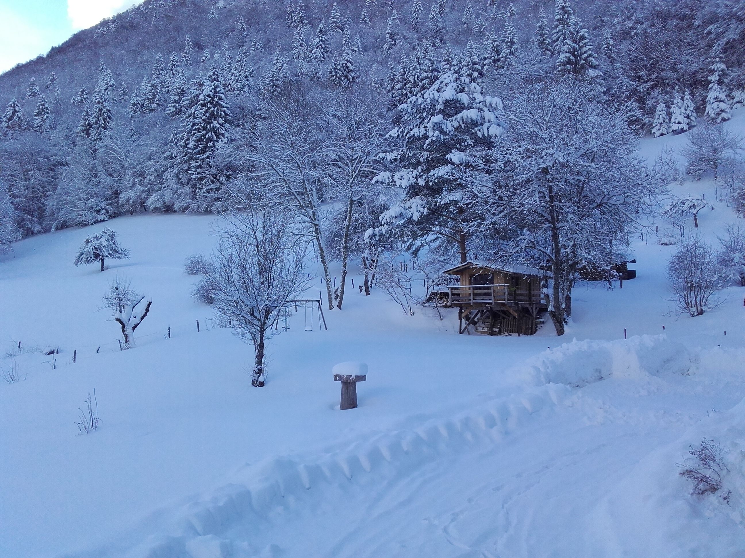 Un paysage enneigé avec une cabane en bois et un portique avec des balançoires.