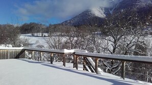 Un paysage enneigé avec une rambarde en bois et une vue sur des arbres et des montagnes recouverts de neige.